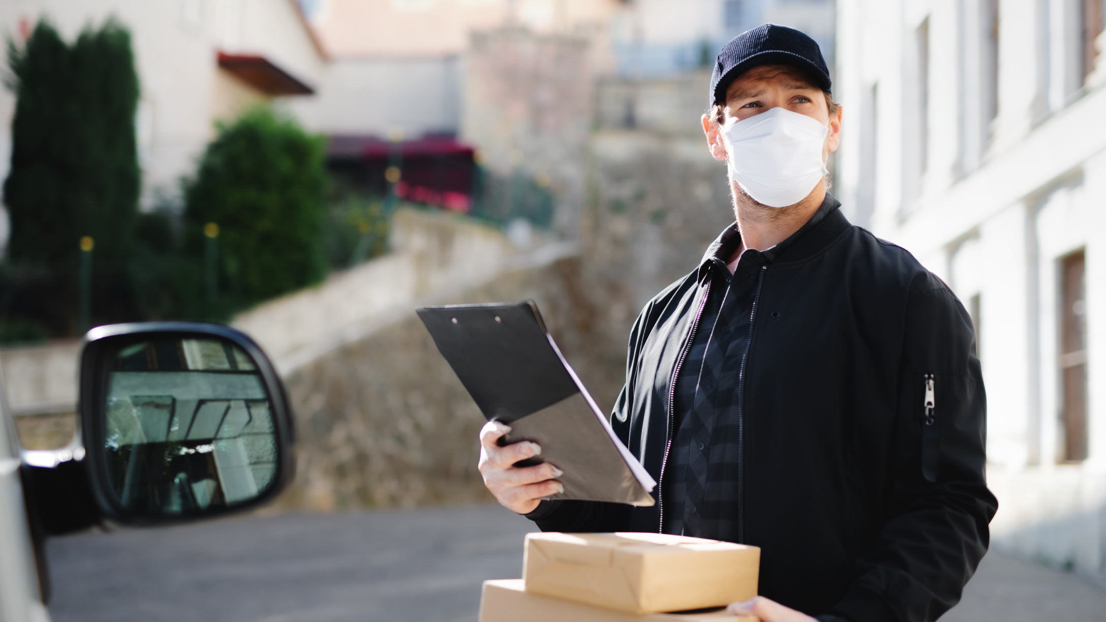 Foto de um reparador com sua pastilha eletrônica e um pacote na mão, em pé em um dia ensolarado em frente ao furgão de entrega.