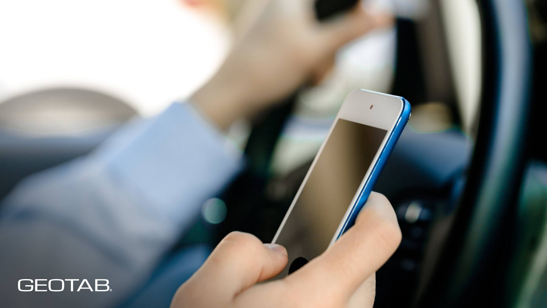 Imagen de persona al volante, escribiendo en un teléfono inteligente que sostiene en la mano