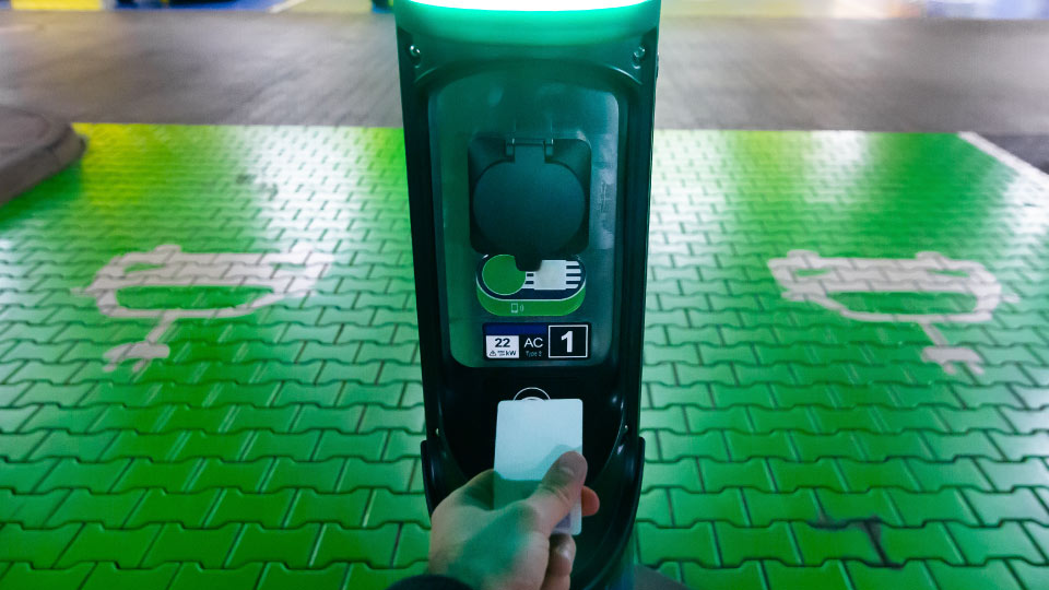Foto de una mano pagando con tarjeta en un estación de carga verde.