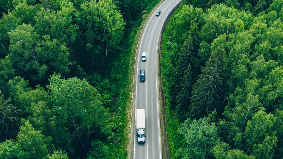 Aerial view of different vehicles driving along a road passing through a forest area