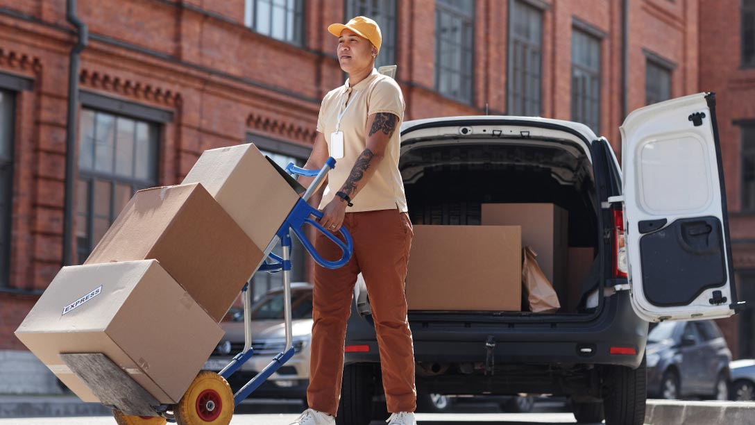 Foto de una mujer transportando tres cajas de una camioneta blanca de última milla.