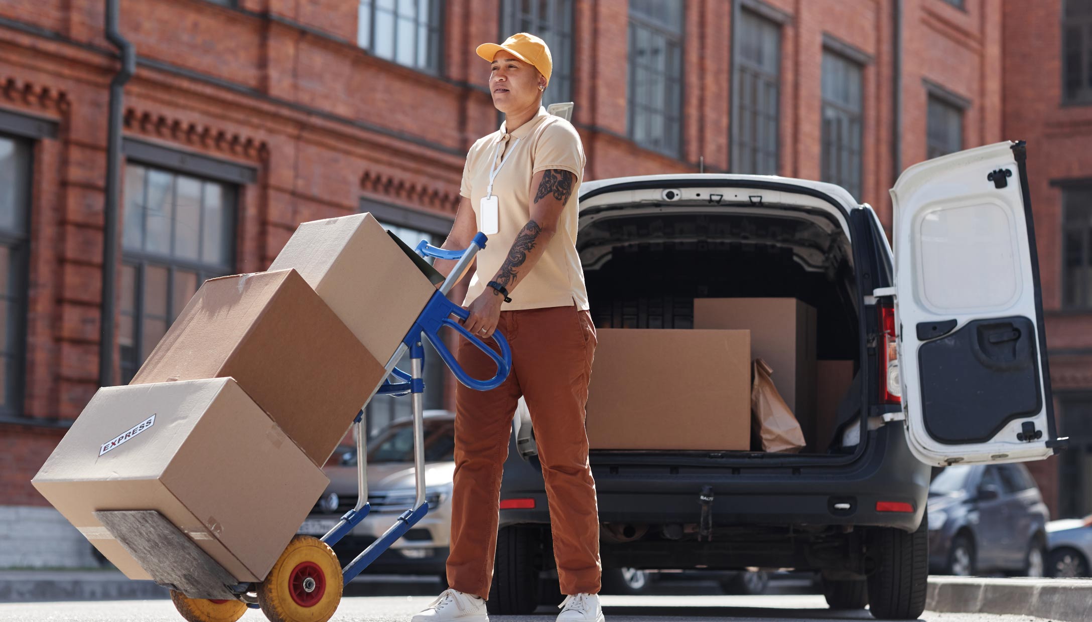 Foto de una mujer transportando tres cajas de una camioneta blanca de última milla.