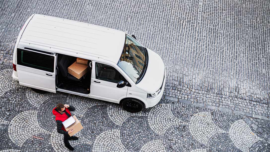 Foto de una camioneta blanca de última milla con un hombre cargando una caja al lado.