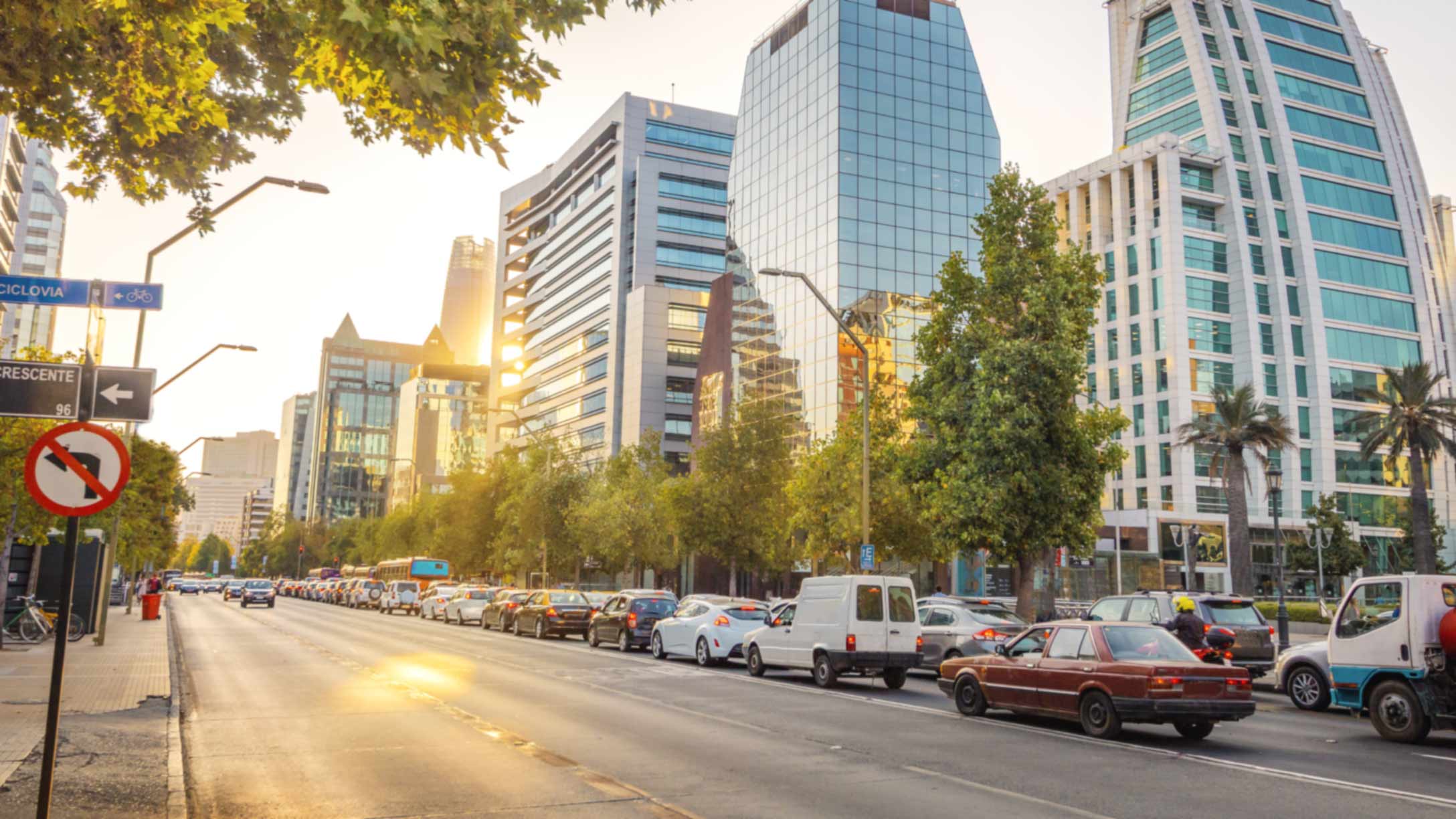 Foto de una carretera con vehículos estacionados a la derecha con edificios en el fondo.