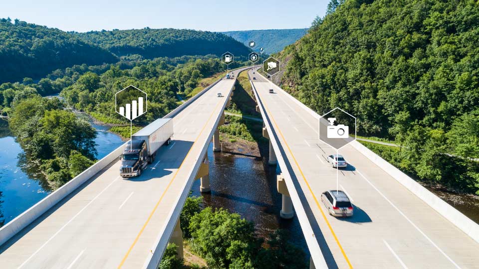 Foto de una carretera doble sobre un lago y un bosque con vehículos y símbolos de datos.