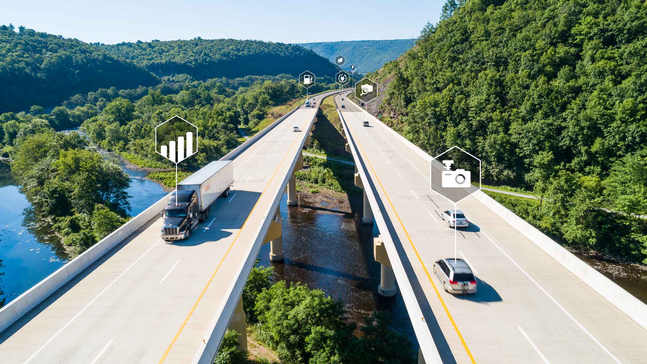 Foto de una carretera doble sobre un lago y un bosque con vehículos y símbolos de datos.