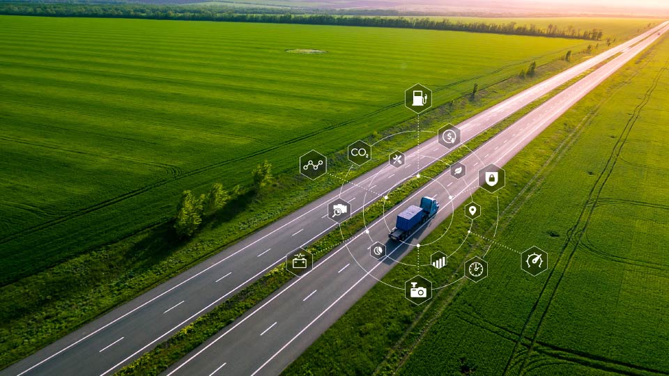 Foto de un camión pesado conduciendo por una carretera en un campo verde con iconos de datos alrededor.