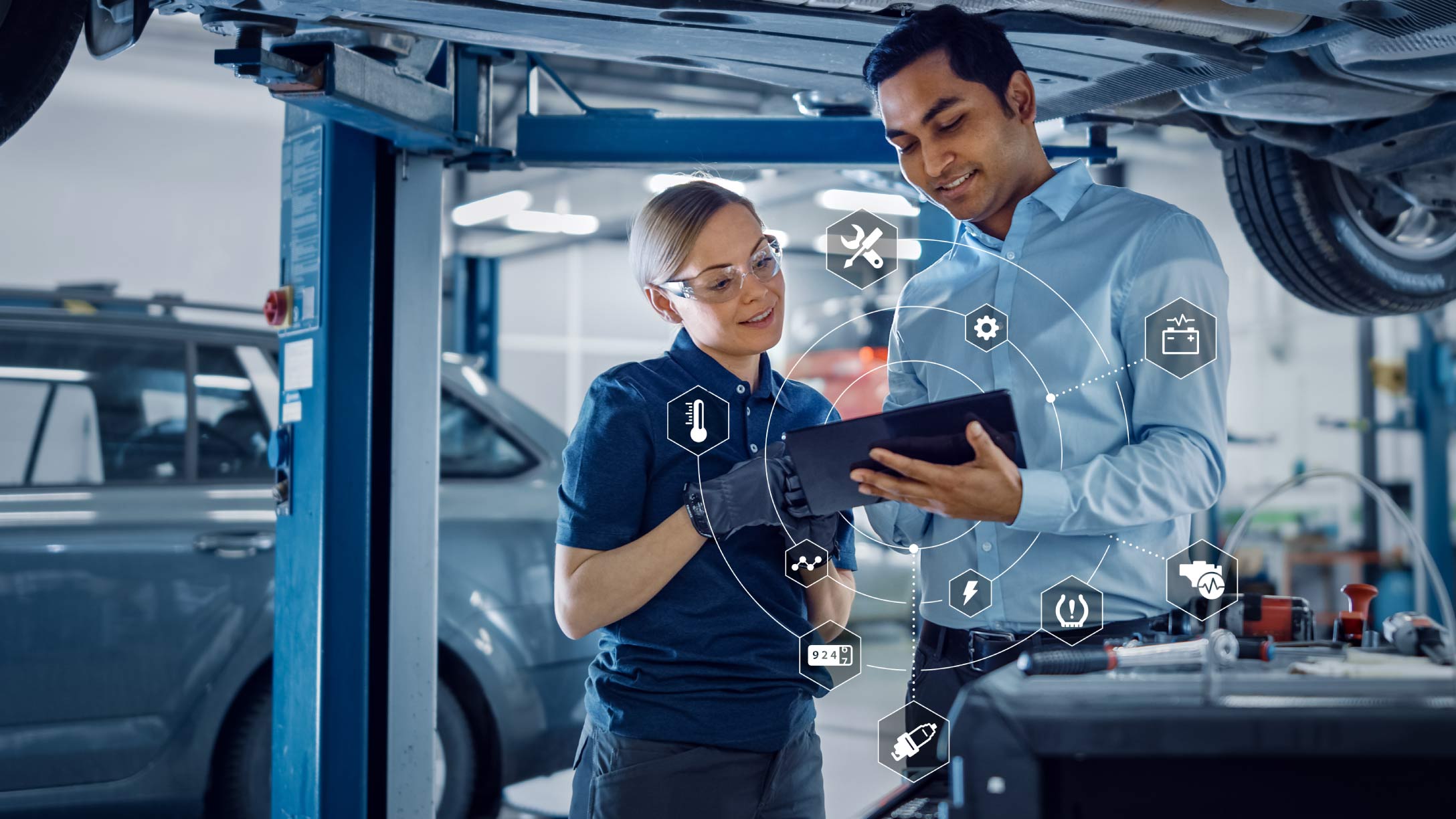 Foto de dos mecánicos trabajando sobre un tablet con símbolos de datos.