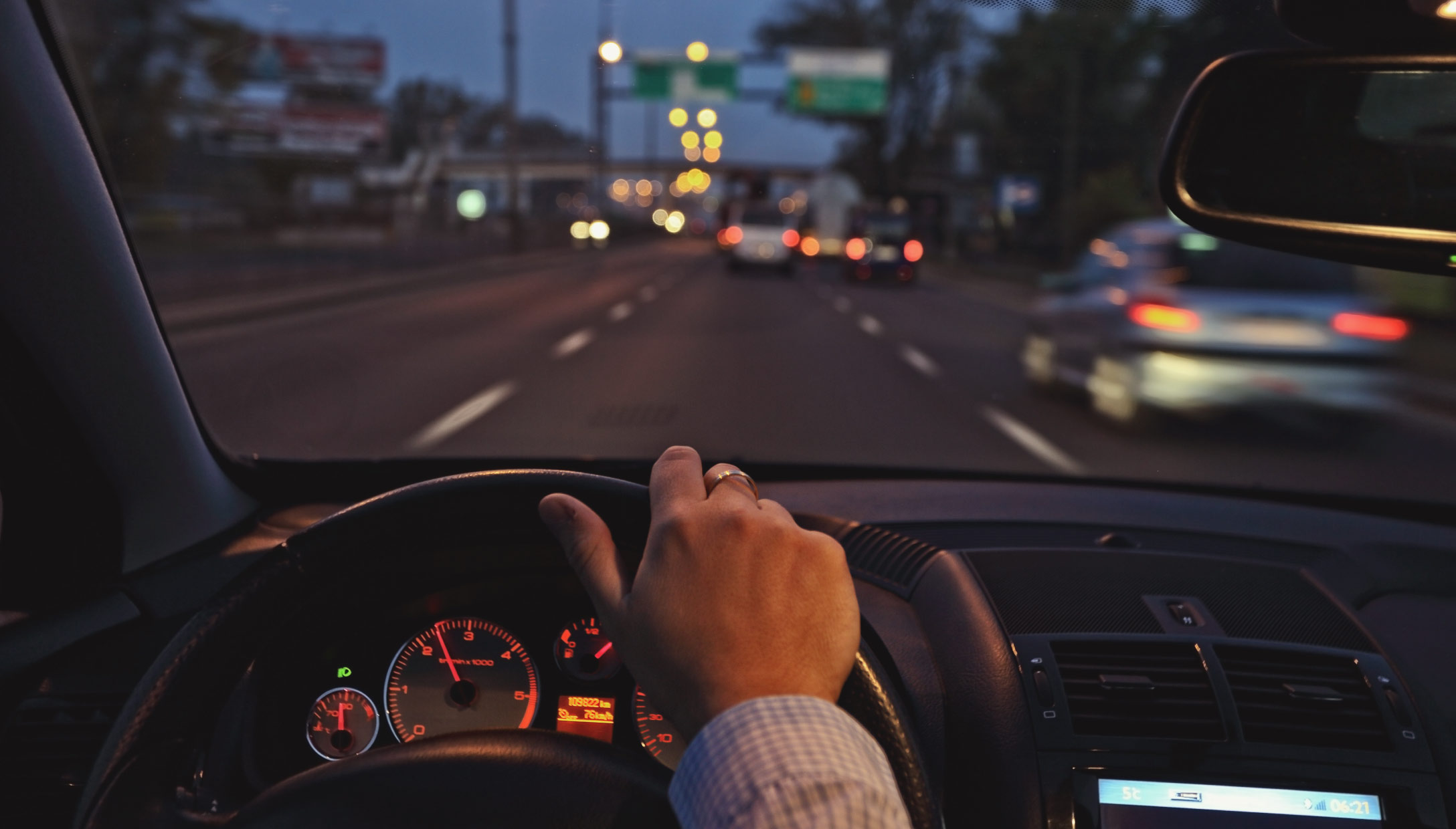 Imagen de una persona conduciendo, con vista de su mano en el volante y la calle enfrente