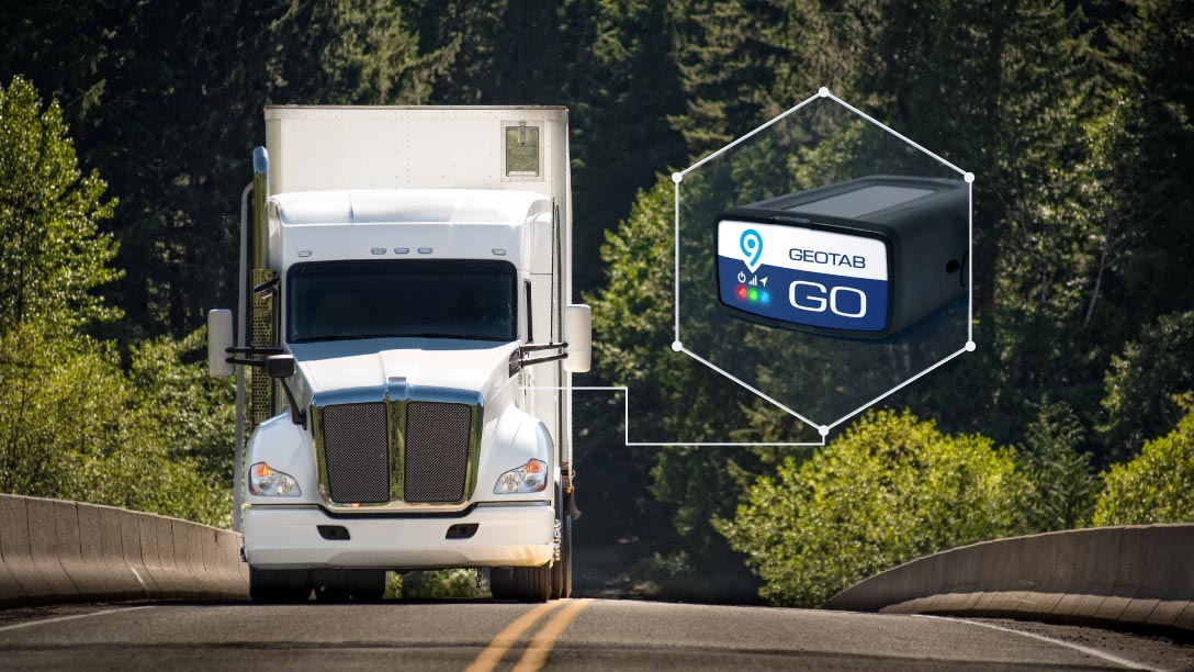 Foto de un camión pesado blanco conduciendo por una carretera rodeada por un bosque con el dispositivo telemático de Geotab, el GO9, al lado.