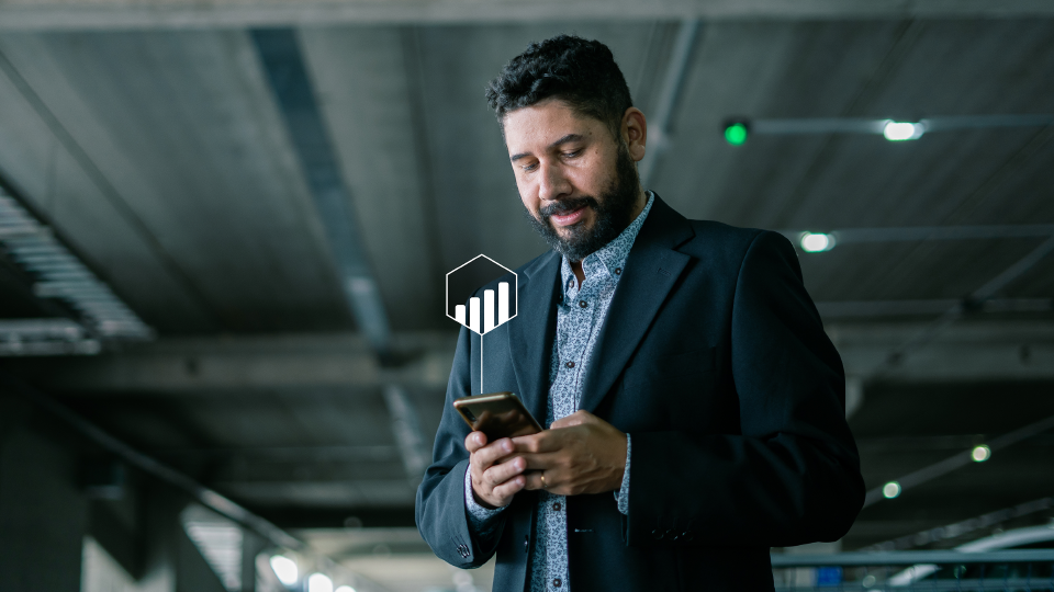 Foto de un hombre en un garage vestido en traje mirando el celular que muestra un icono de datos.