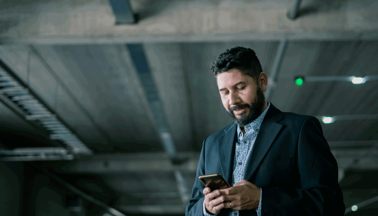 Foto de un hombre en un garage vestido en traje mirando el celular.