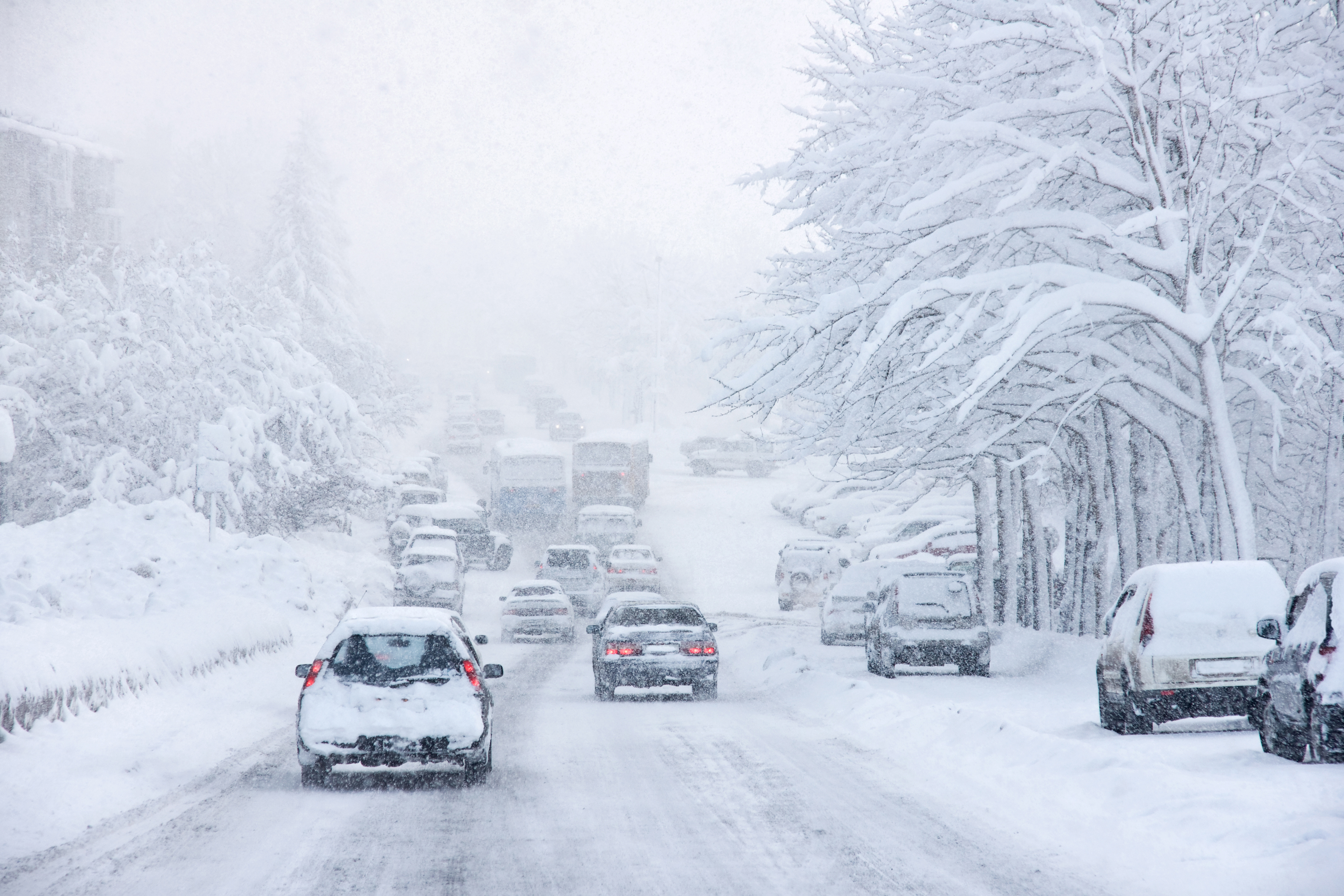 Tráfico de vehículos y camiones avanzando lentamente durante una intensa tormenta de nieve con baja visibilidad, ilustrando los desafíos climáticos para las flotas en invierno.