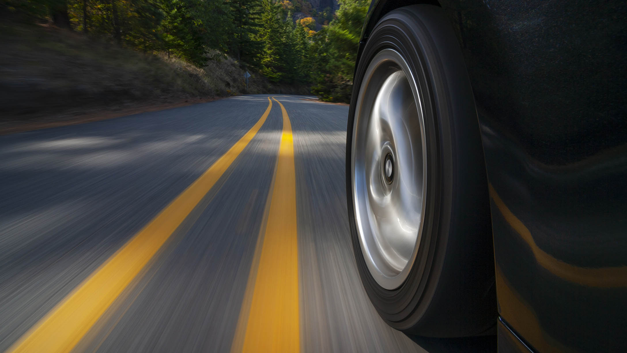 Foto de un neumático de un vehículo eléctrico conduciendo por una carretera rodeada por árboles durante el día.
