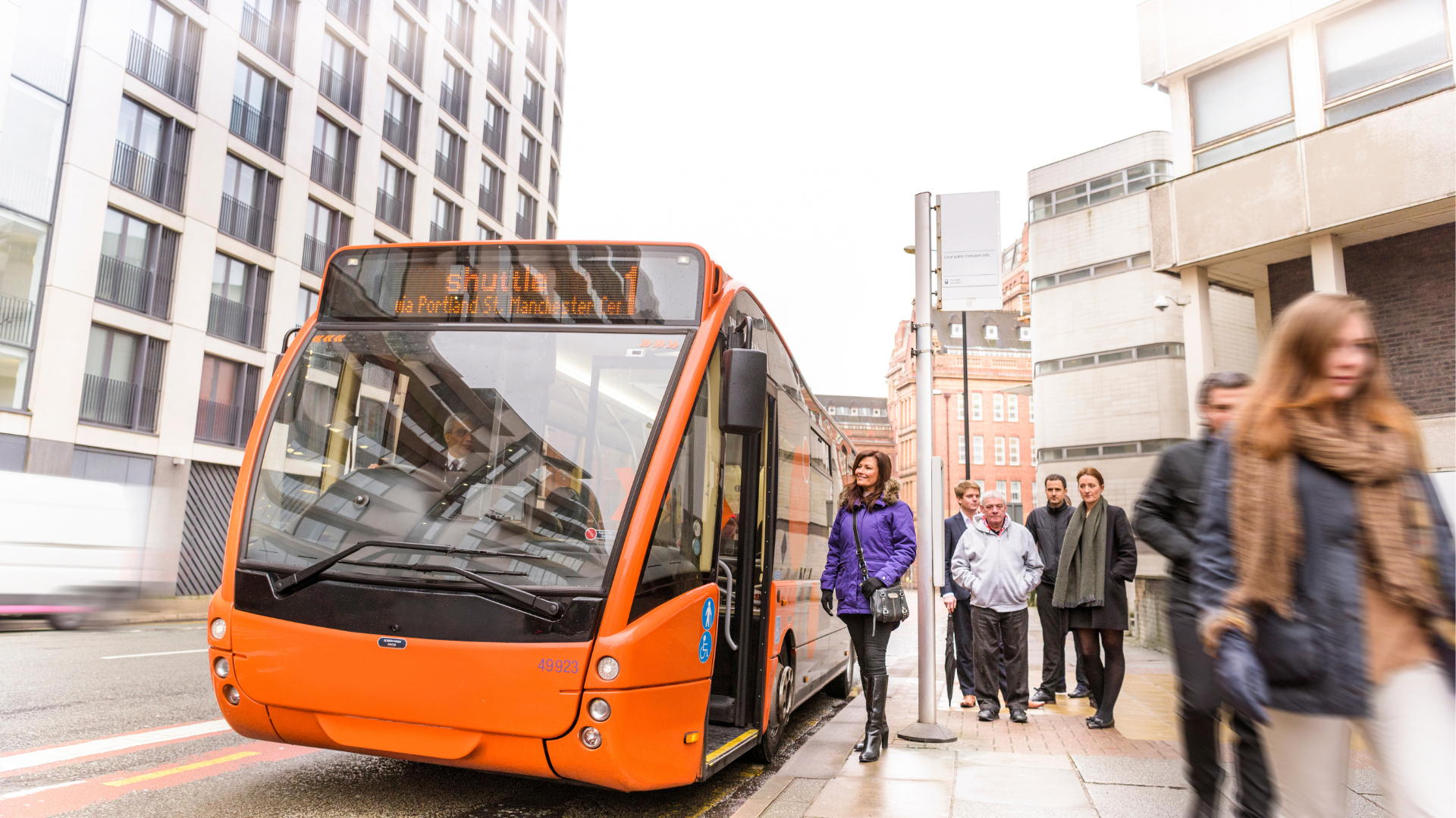 Orange single-decker bus arriving at a city bus stop.