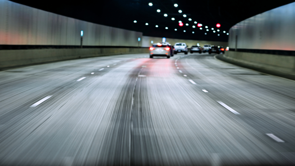 Une vue dashcam en flou de mouvement, montrant la conduite dans un tunnel autoroutier sombre la nuit, en suivant la circulation.