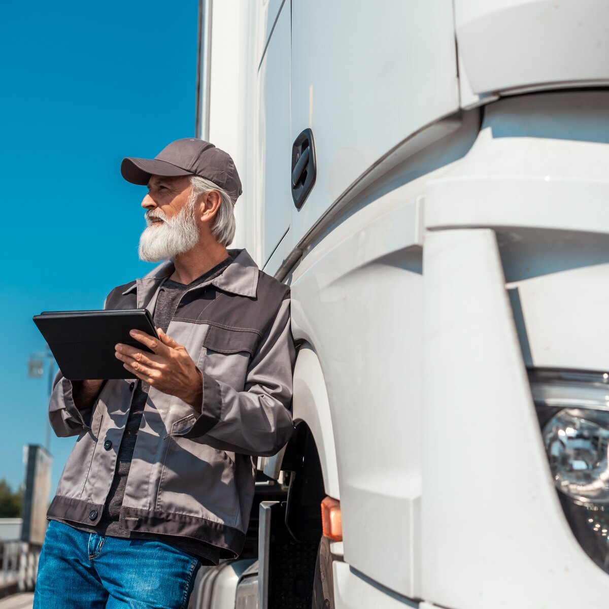 Chauffeur de camion senior, appuyé contre son camion blanc tout en tenant une tablette.