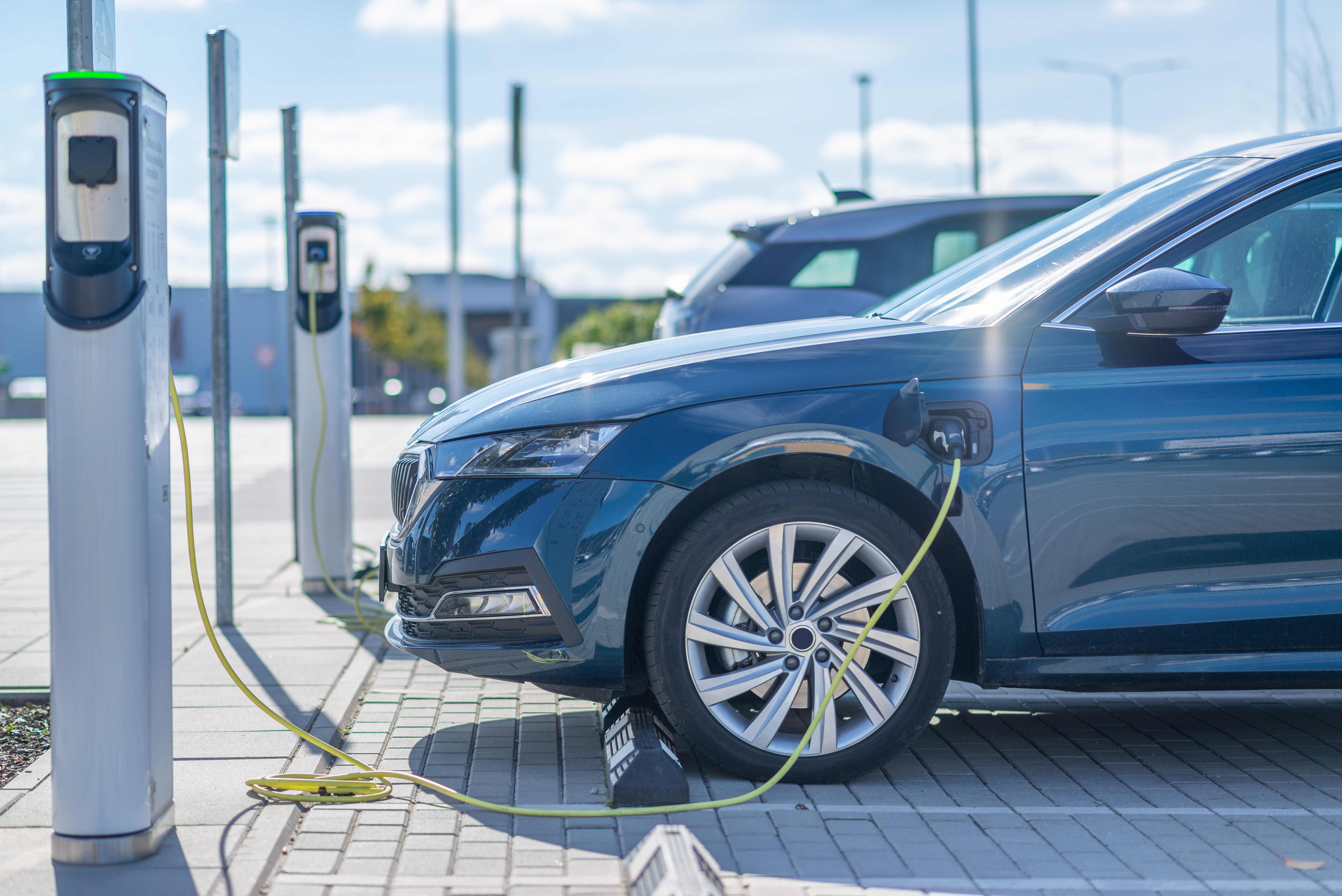 A blue electric vehicle charging with a cable at an outdoor charging station.