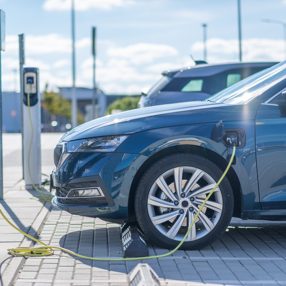 A blue electric vehicle charging with a cable at an outdoor charging station.