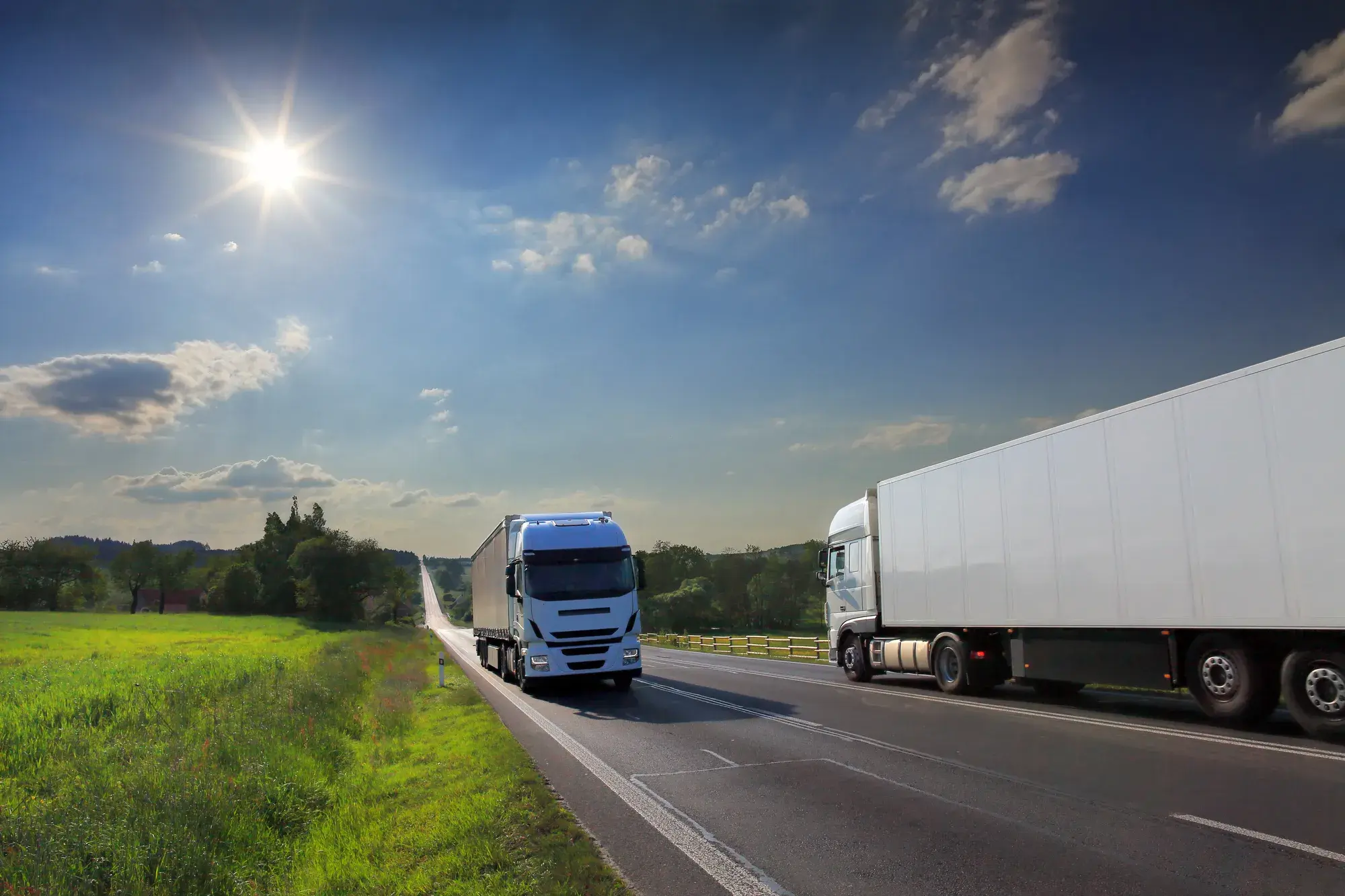 Deux camions sur une autoroute, sous un ciel bleu ensoleillé et entourés de verdure.