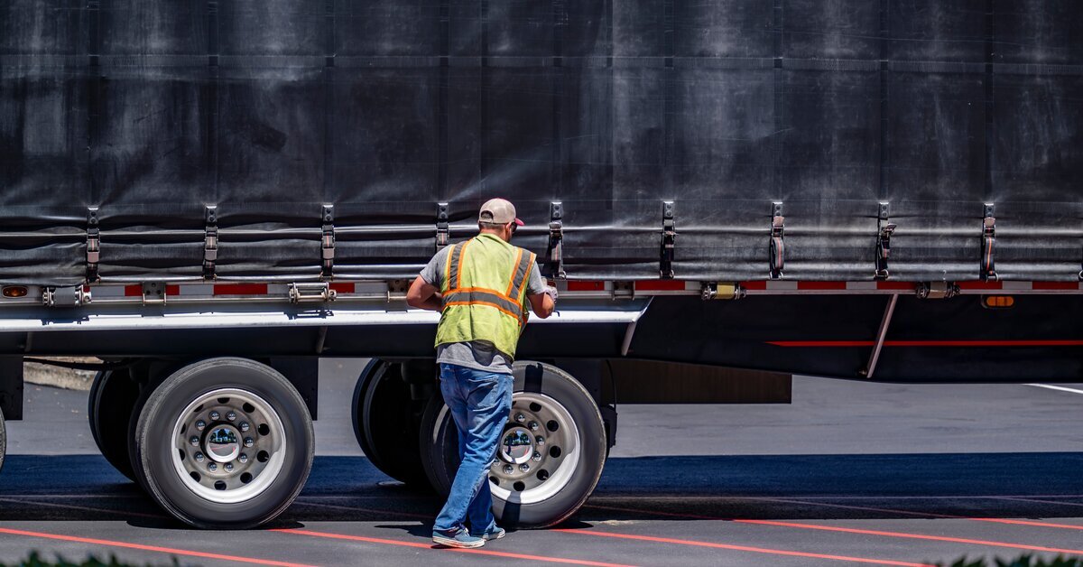 Ouvrier devant un gros camion avec son gilet jaune.