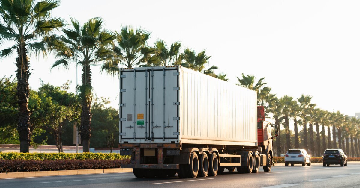 Gros camion et deux voitures sur la route à côté d'arbres.
