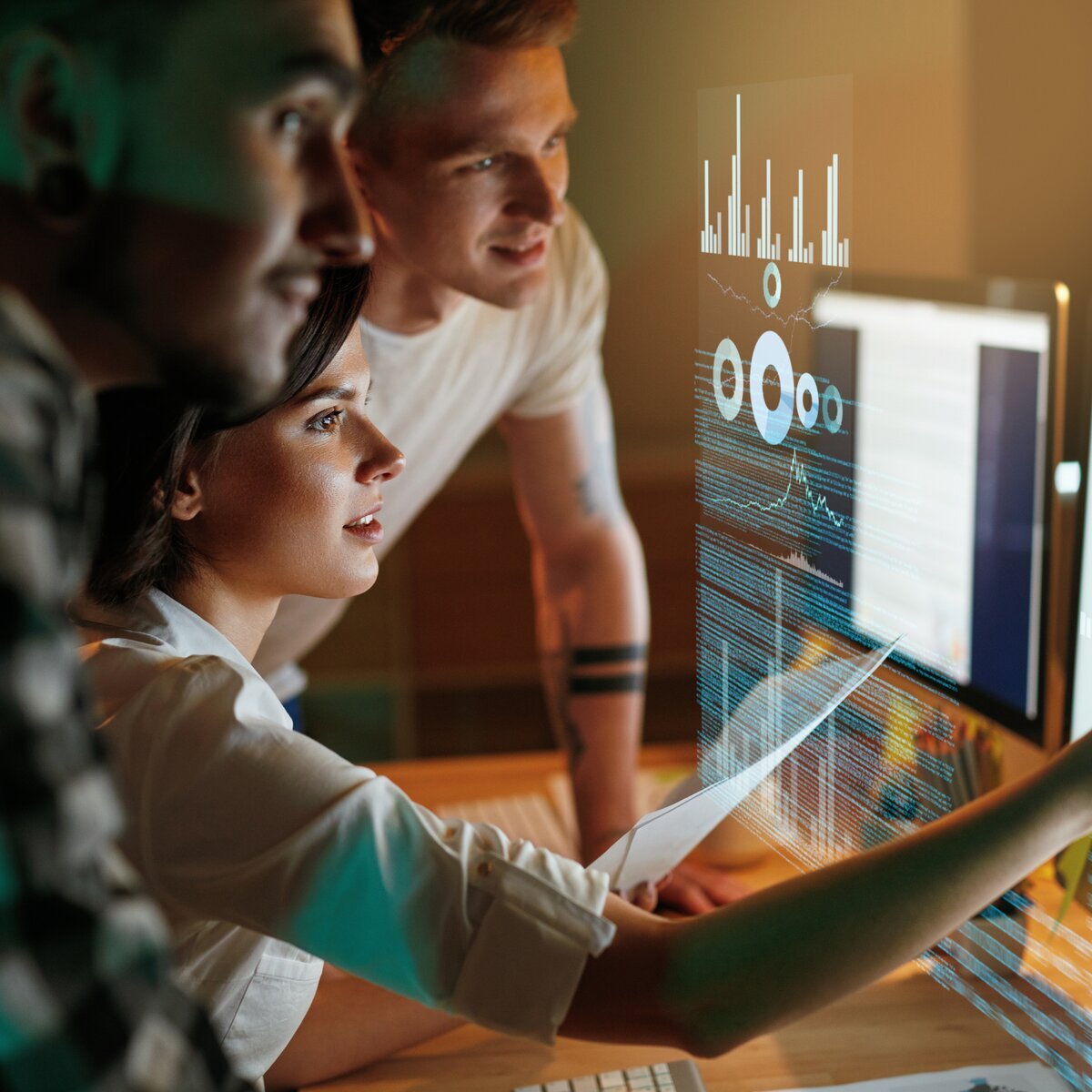 Trois personnes regardant et analysant des données sur un écran d'ordinateur, avec des graphiques.