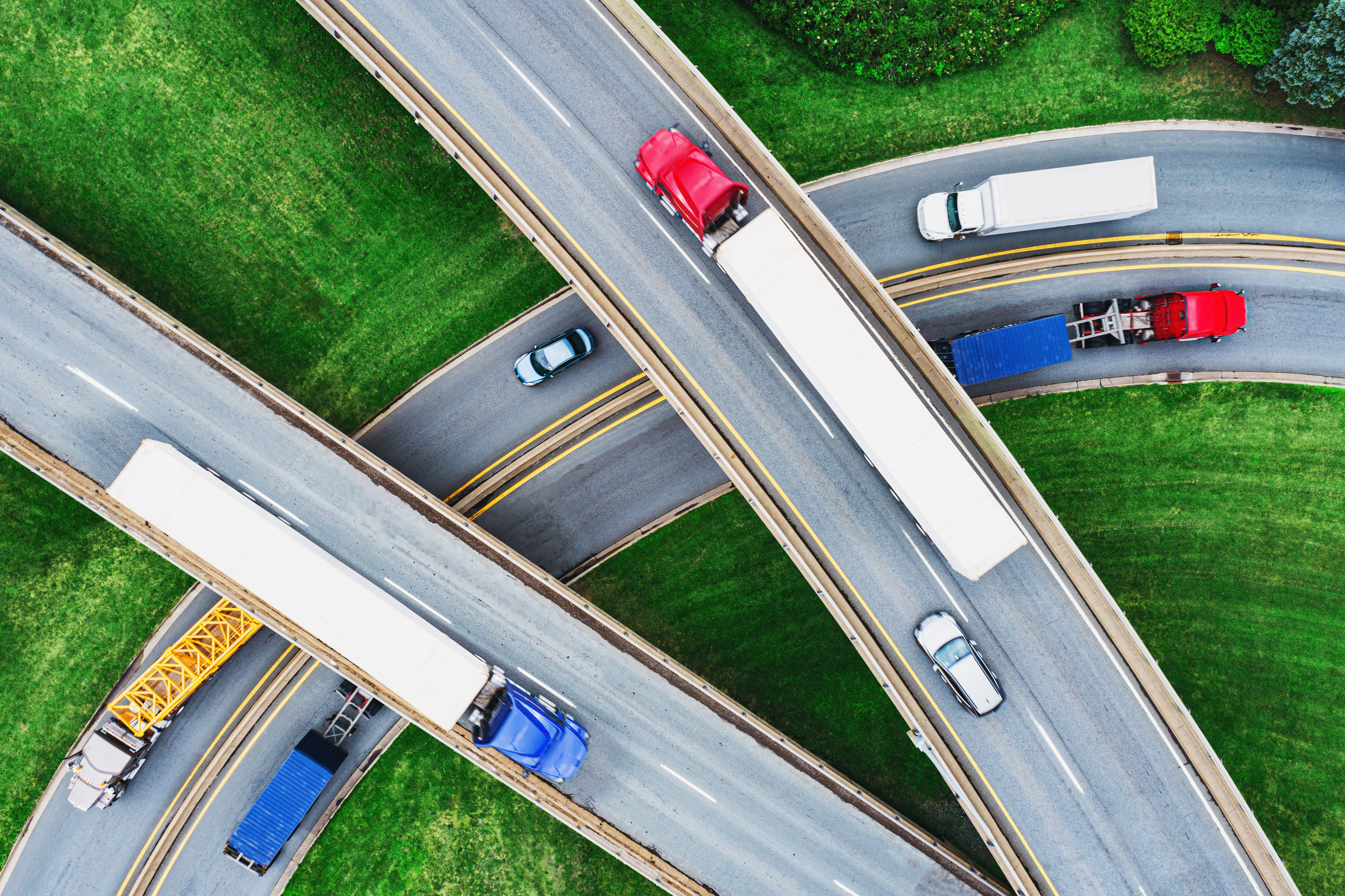 Vue aérienne d'un échangeur autoroutier et de ses bretelles, montrant plusieurs camions de transport et quelques voitures qui circulent.