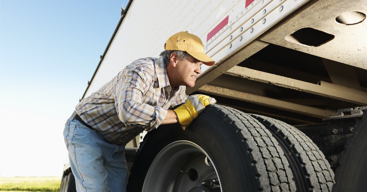 Homme qui regarde au-dessus du pneu d'un camion blanc.