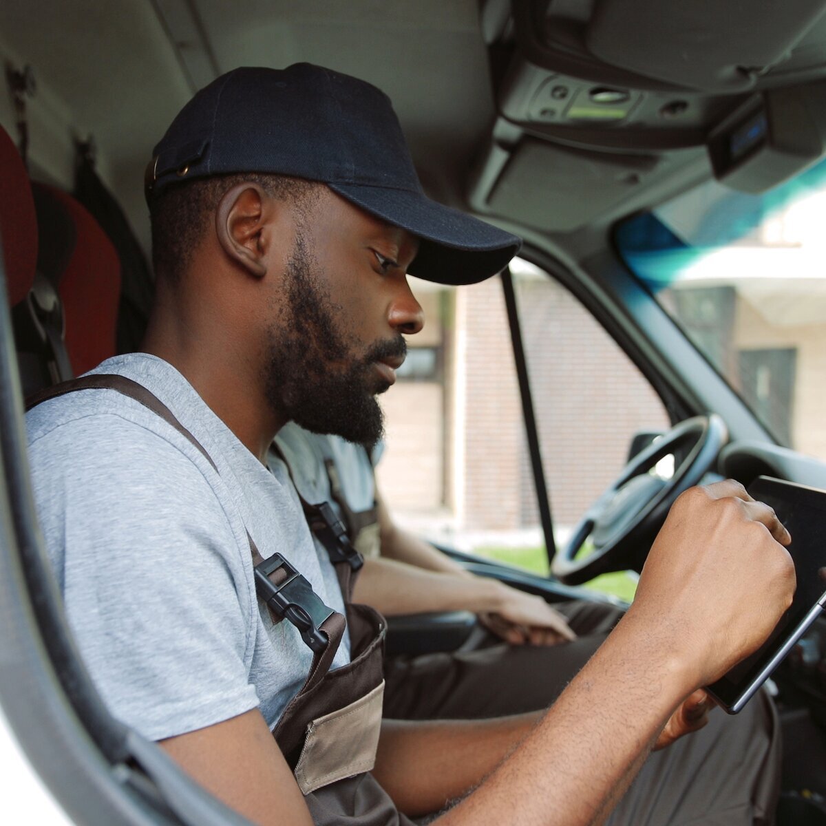 Un chauffeur assis dans un véhicule, regardant une tablette numérique dans ses mains.