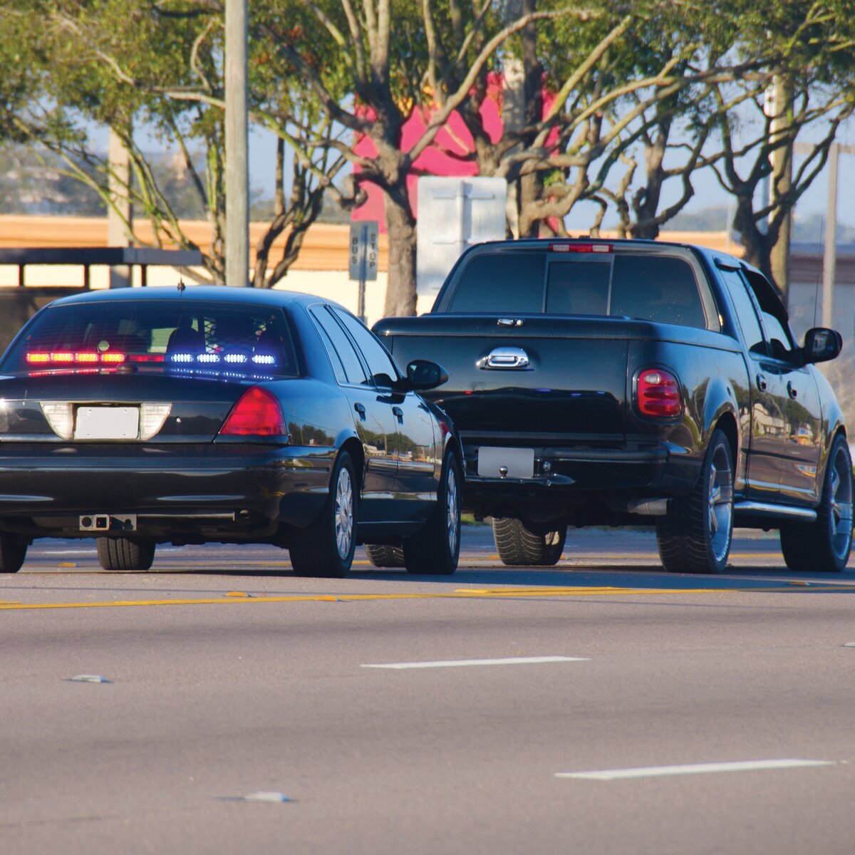 Une voiture de police noire avec des gyrophares allumés, suivie de près par un pick-up noir, roulant sur une route.