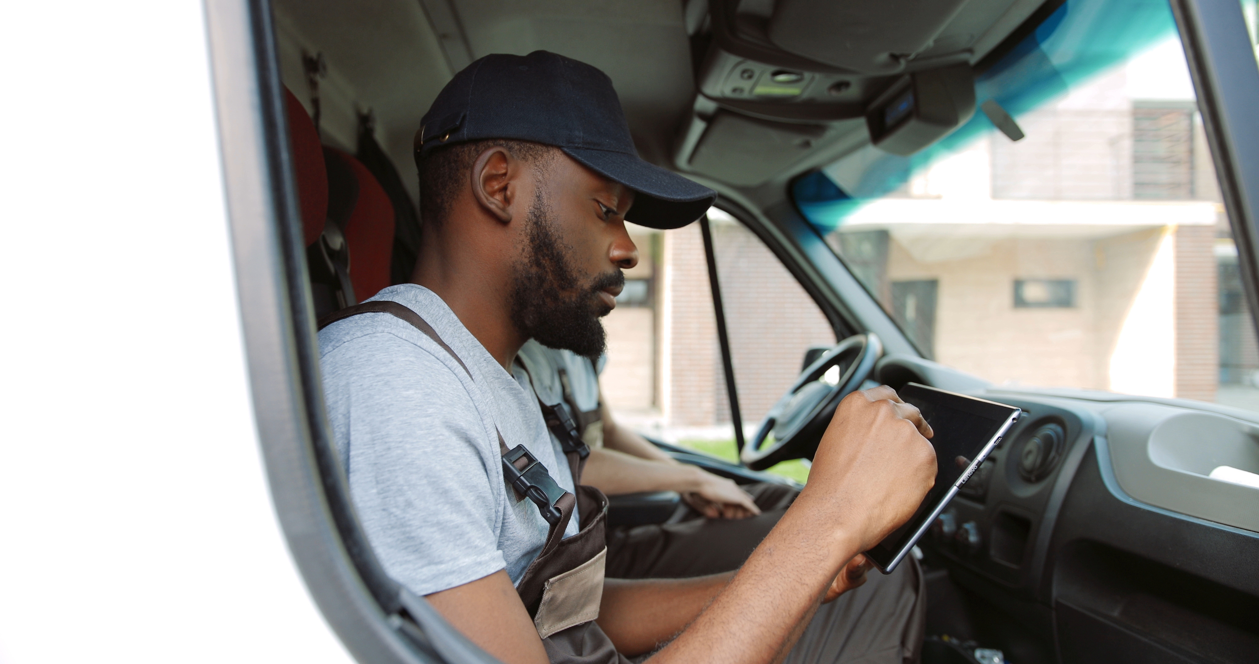 Un chauffeur assis dans un véhicule, regardant une tablette numérique dans ses mains.