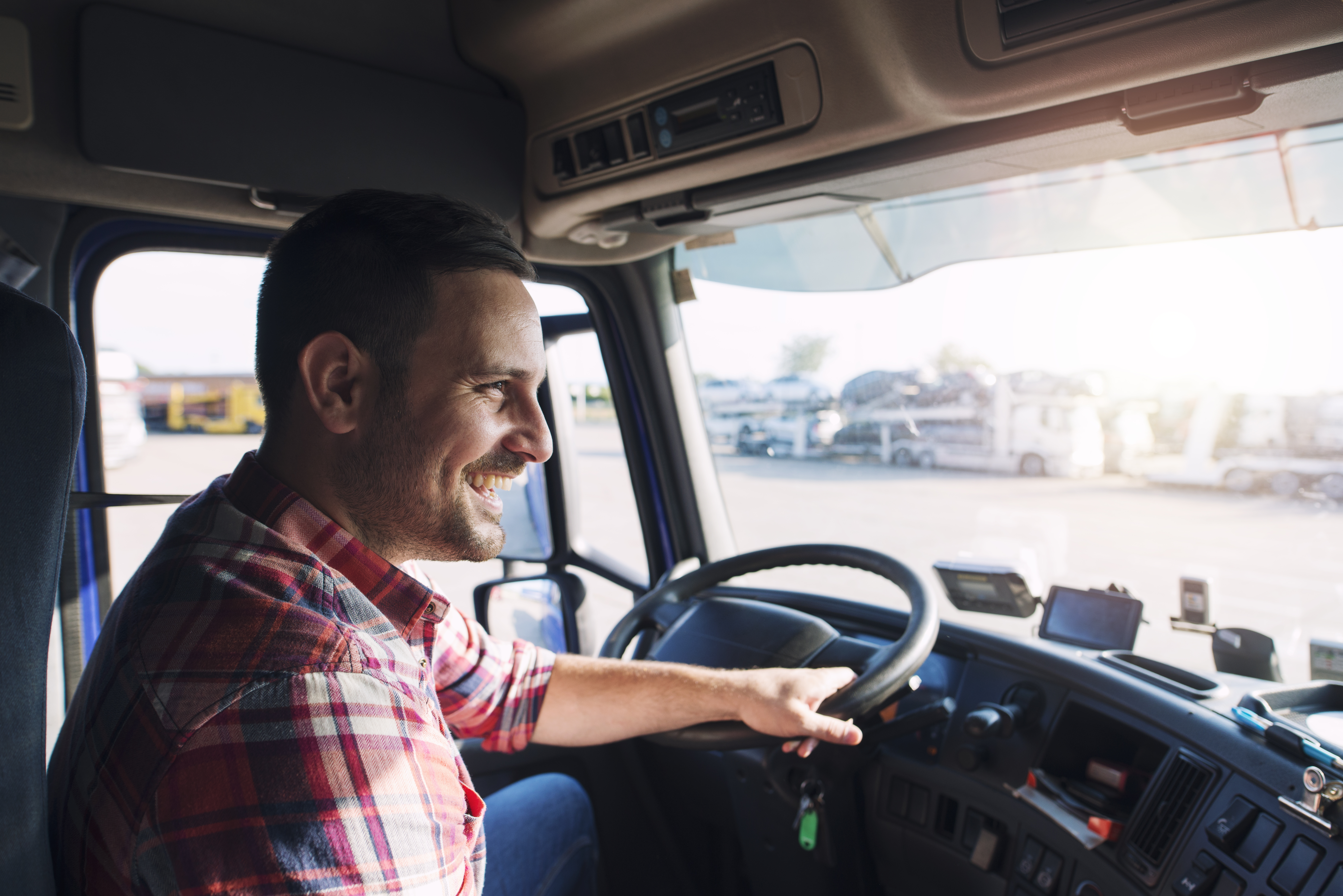 Un chauffeur de camion souriant au volant, en plein soleil.