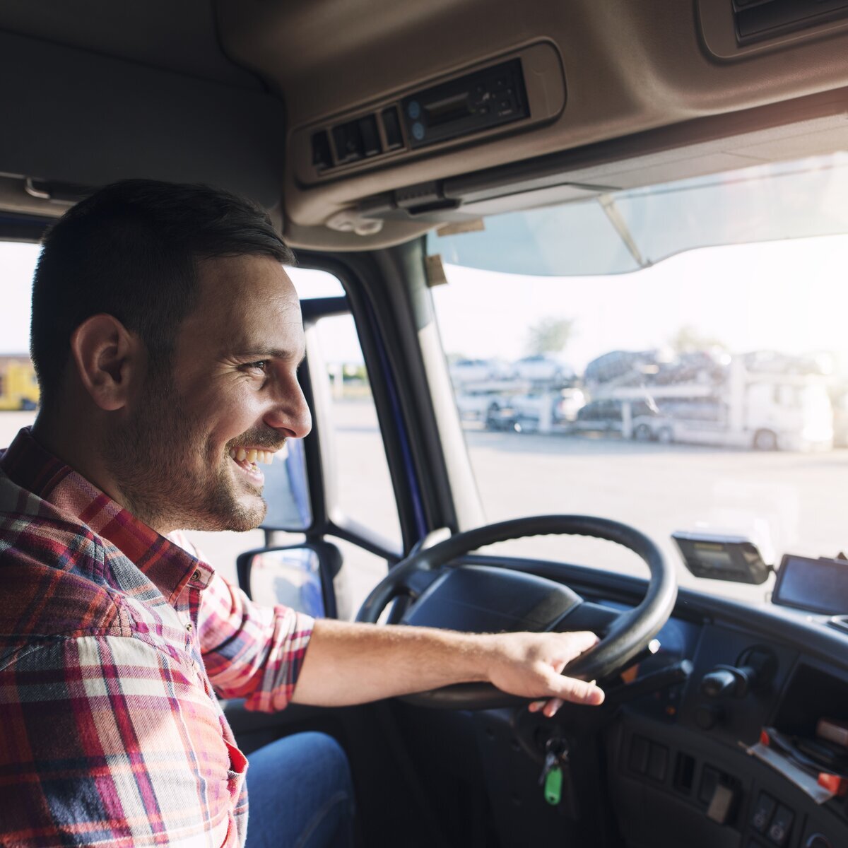 Un chauffeur de camion souriant au volant, en plein soleil.