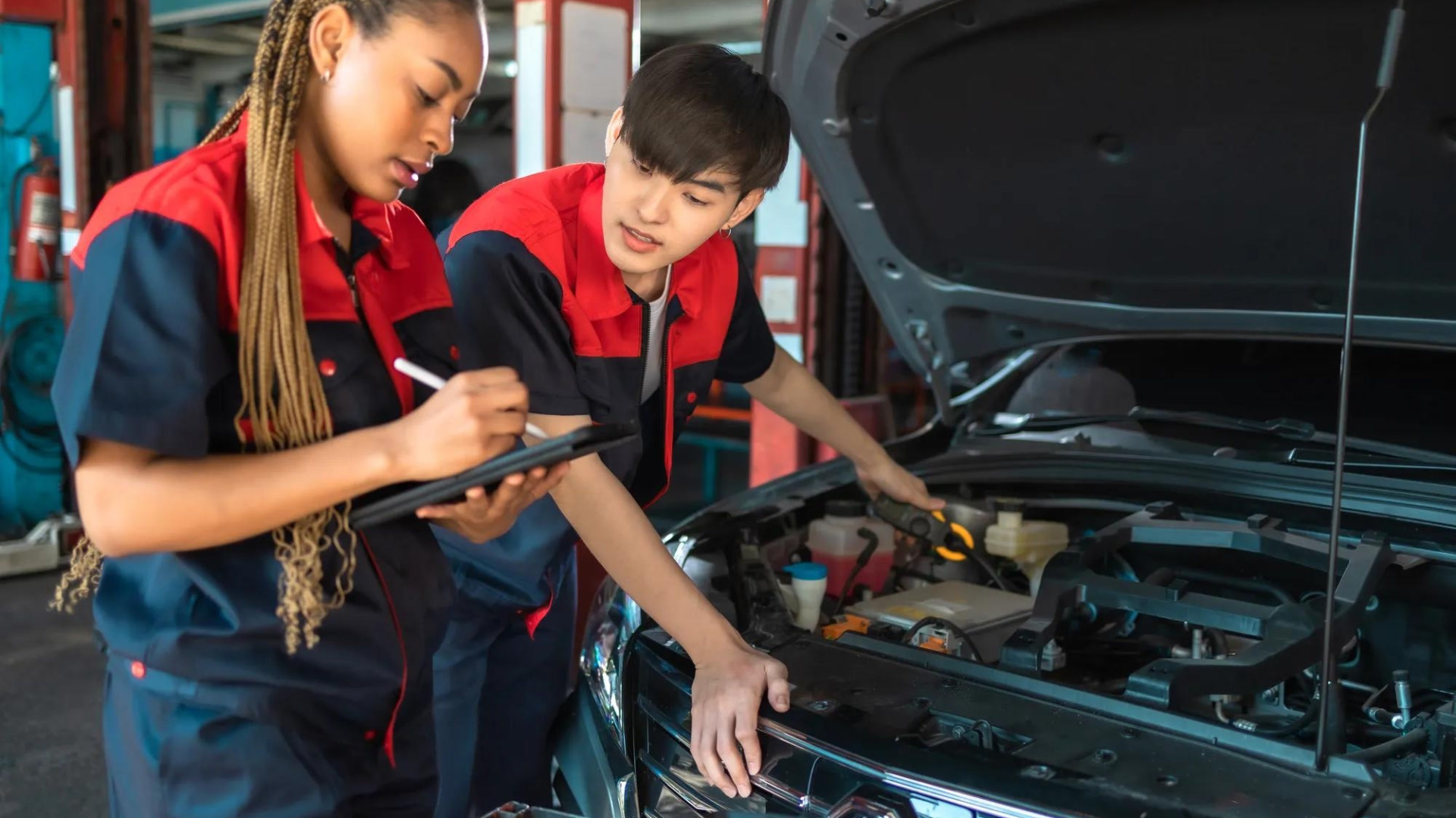 Deux mécaniciens en uniforme rouge et bleu inspectent le moteur d'une voiture dans un atelier