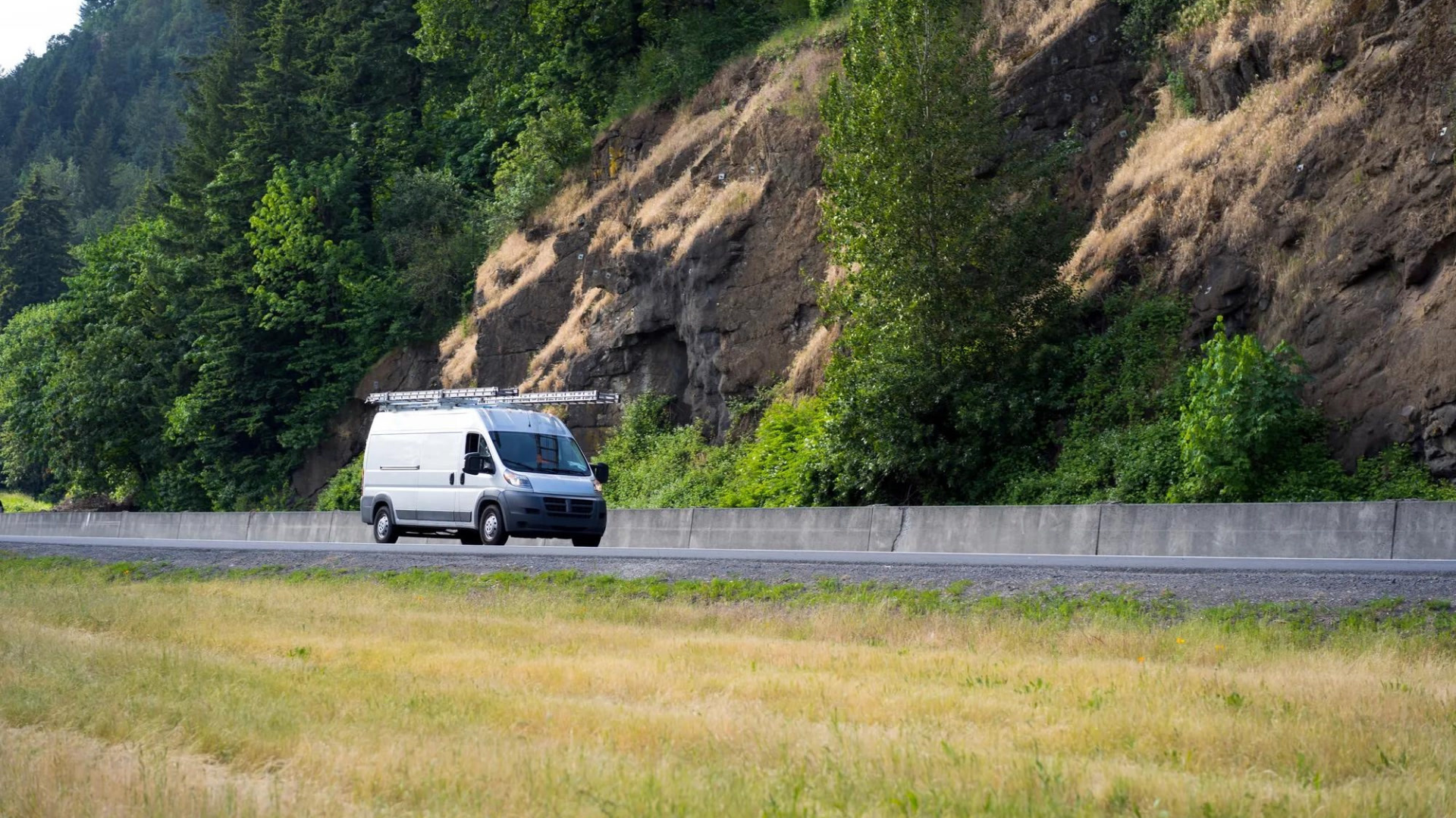 Un fourgon blanc circulant sur une autoroute avec des falaises rocheuses et de la végétation en arrière-plan