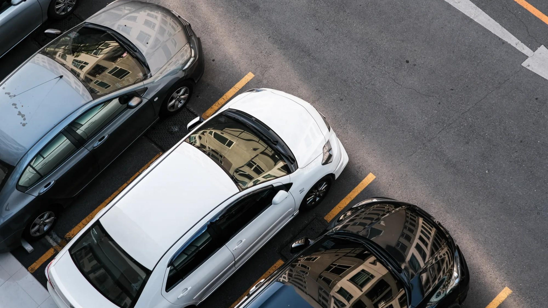 Vue aérienne de trois voitures garées dans un parking avec des places délimitées par des lignes jaunes