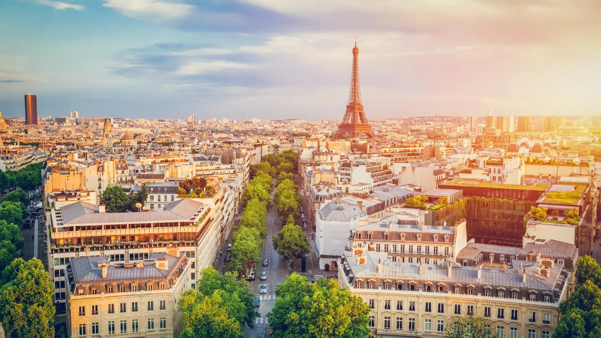 Vue aérienne de Paris avec la Tour Eiffel illuminée au coucher de soleil, entourée de bâtiments haussmanniens et d'arbres verts