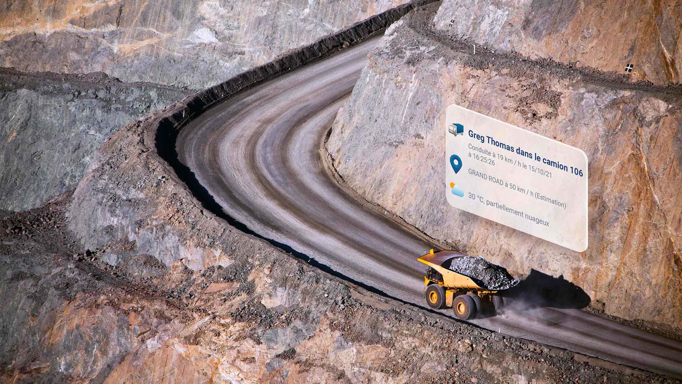 Yellow dump truck driving up a curving dirt road with MyGeotab UI elements above it