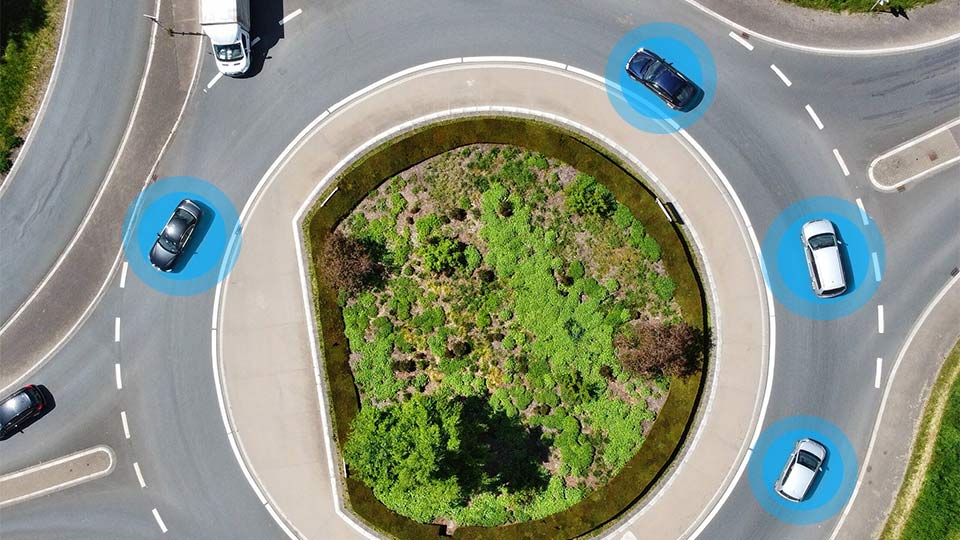 Vari veicoli connessi percorrono una rotatoria con al centro del verde