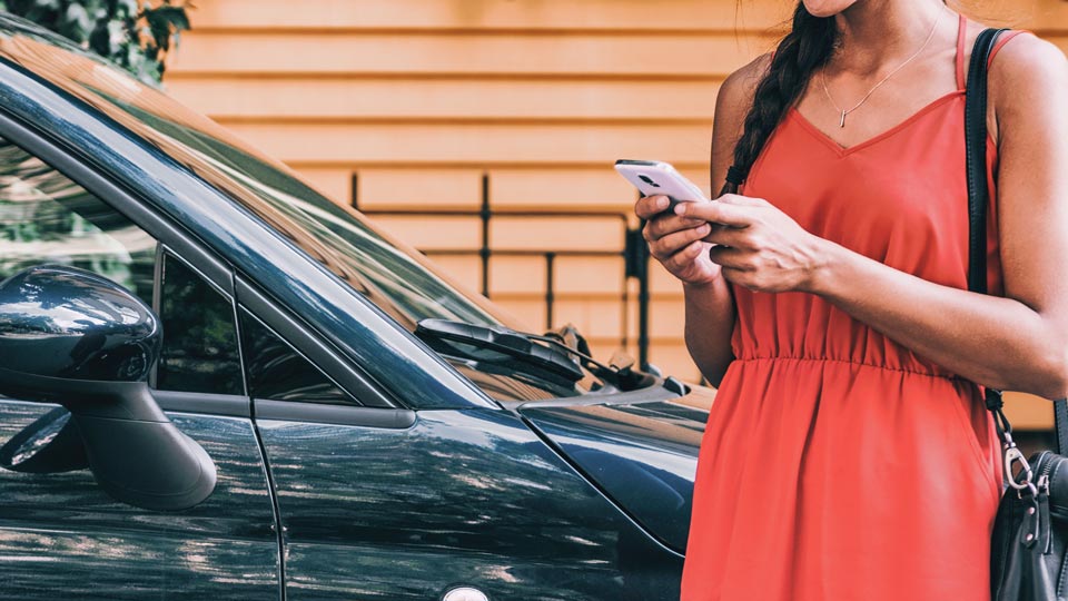 Frau, die außerhalb des Autos steht und ihr Telefon trägt