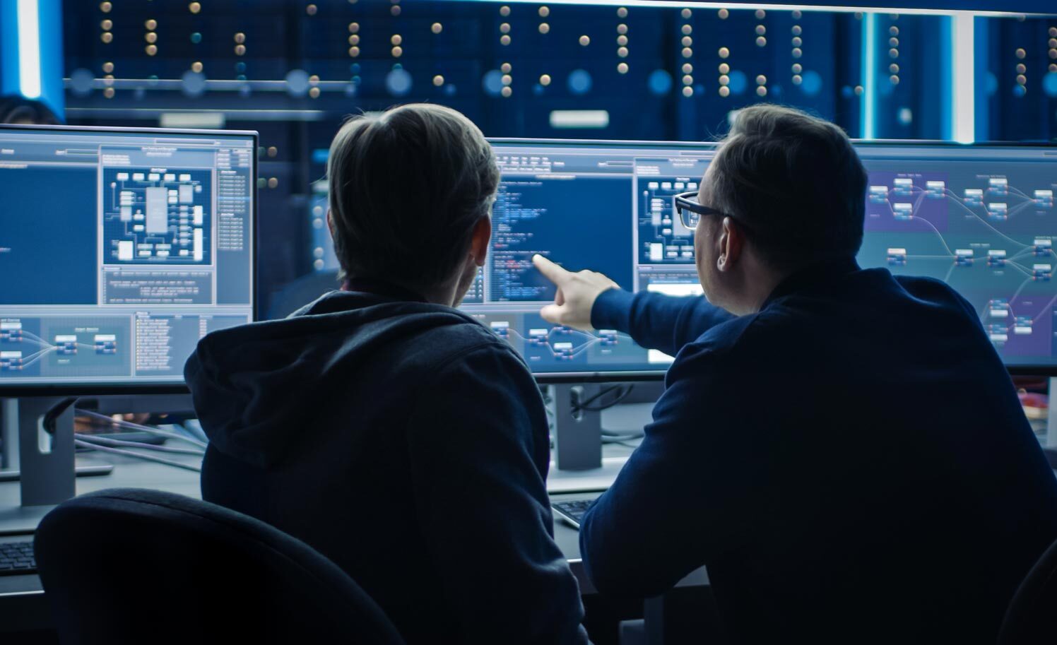 Two analysts reviewing fleet data across multiple monitors in a network operations centre.