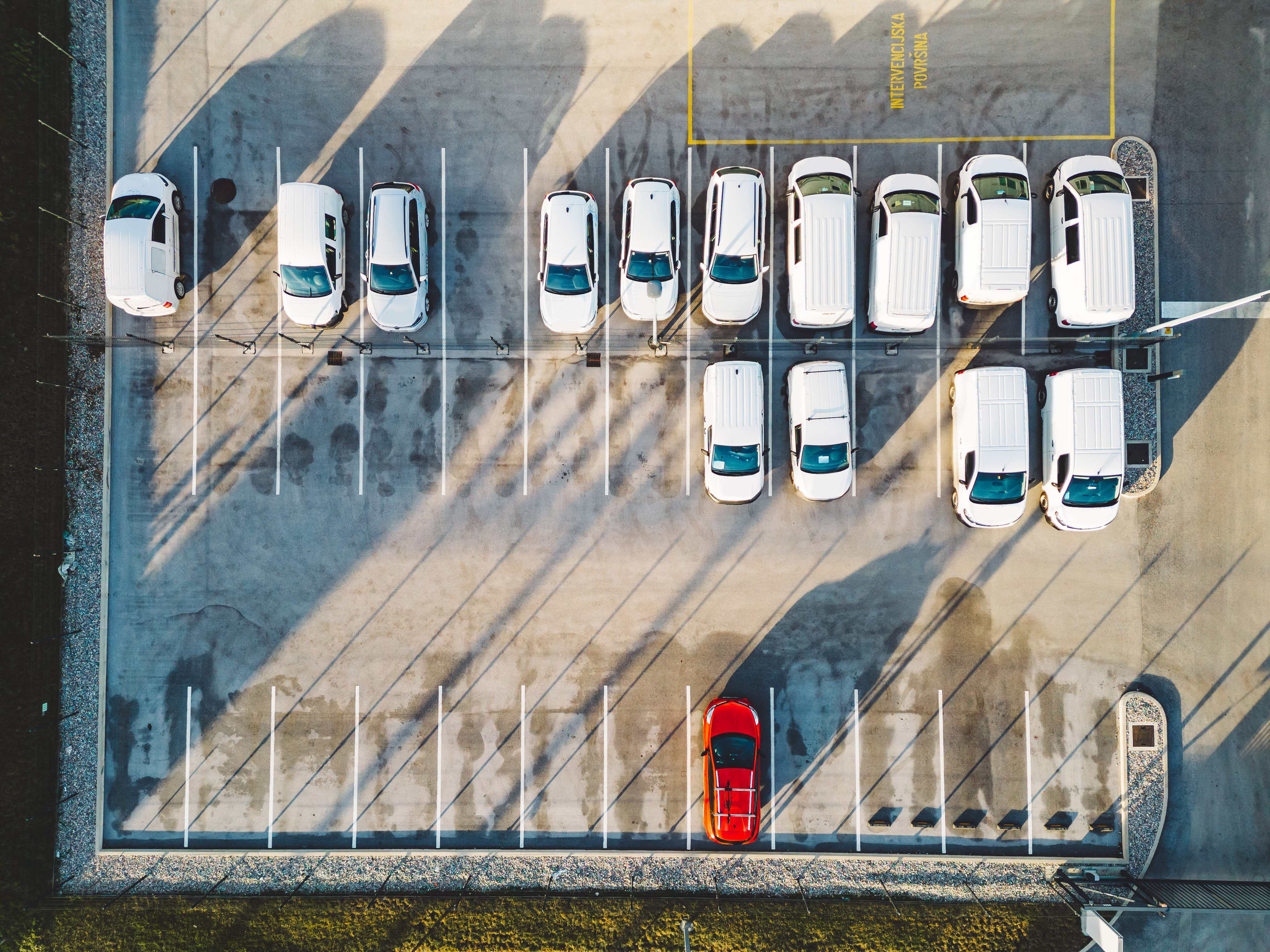 Aerial view of a parking lot featuring rows of white delivery vans with a single red car standing out in contrast.