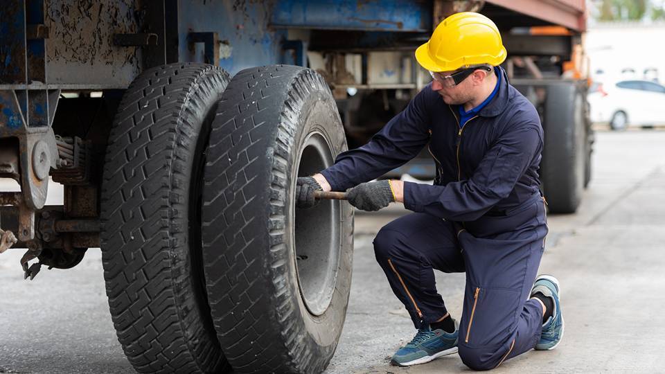 Operaio con DPI che esegue la manutenzione su un pneumatico di un veicolo commerciale pesante.