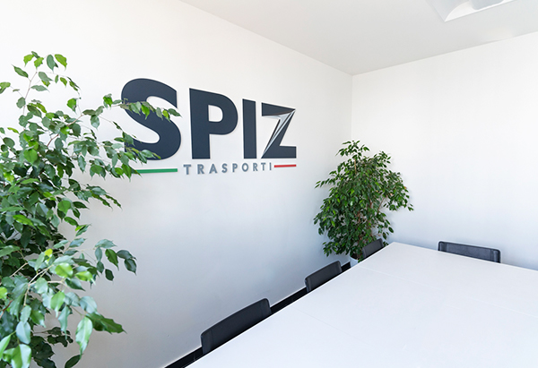 Ufficio di Spiz Trasporti con il logo sul muro bianco e una pianta a lato