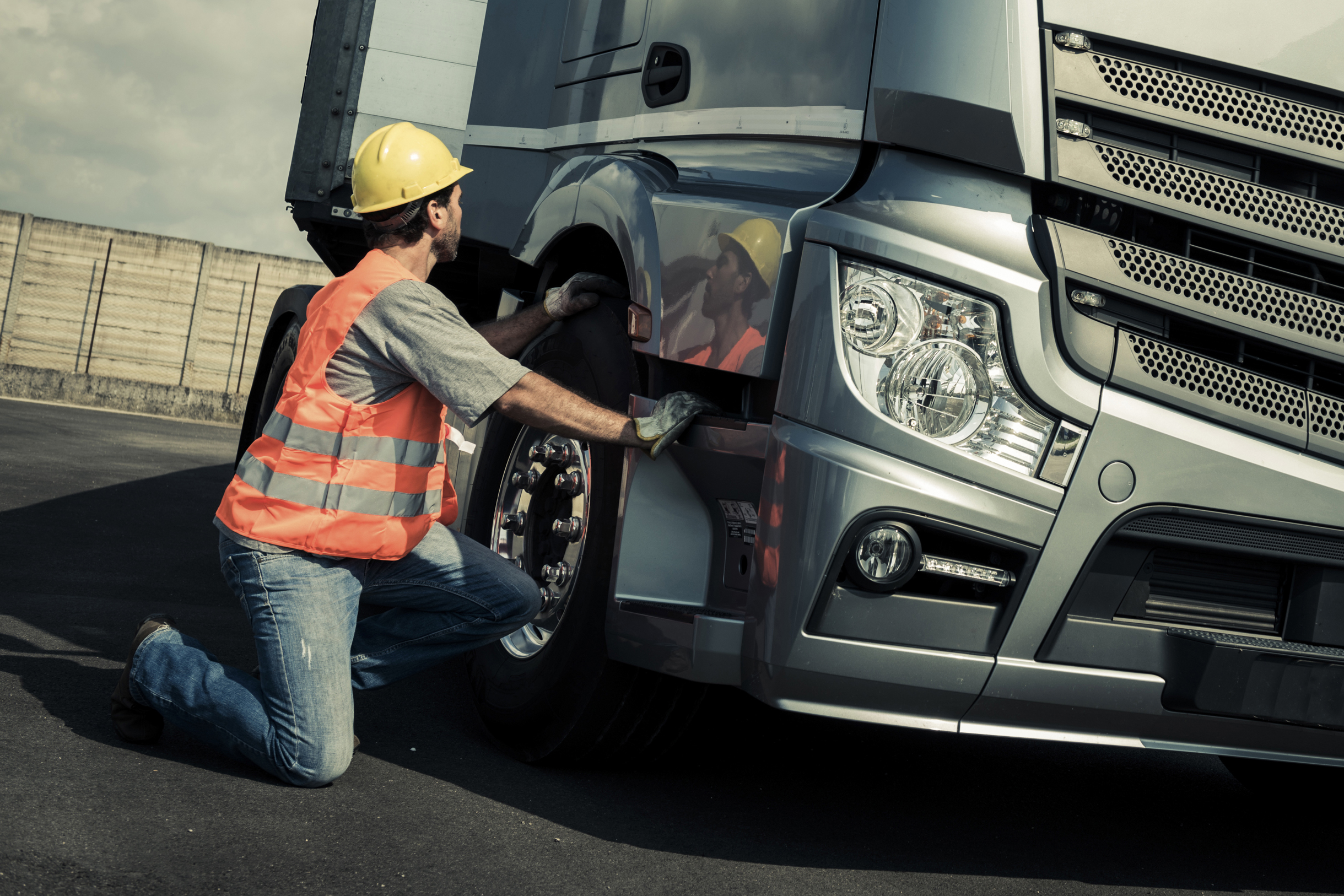 Immagine di un tecnico con casco giallo e gilet arancione che controlla la ruota di un camion fermo