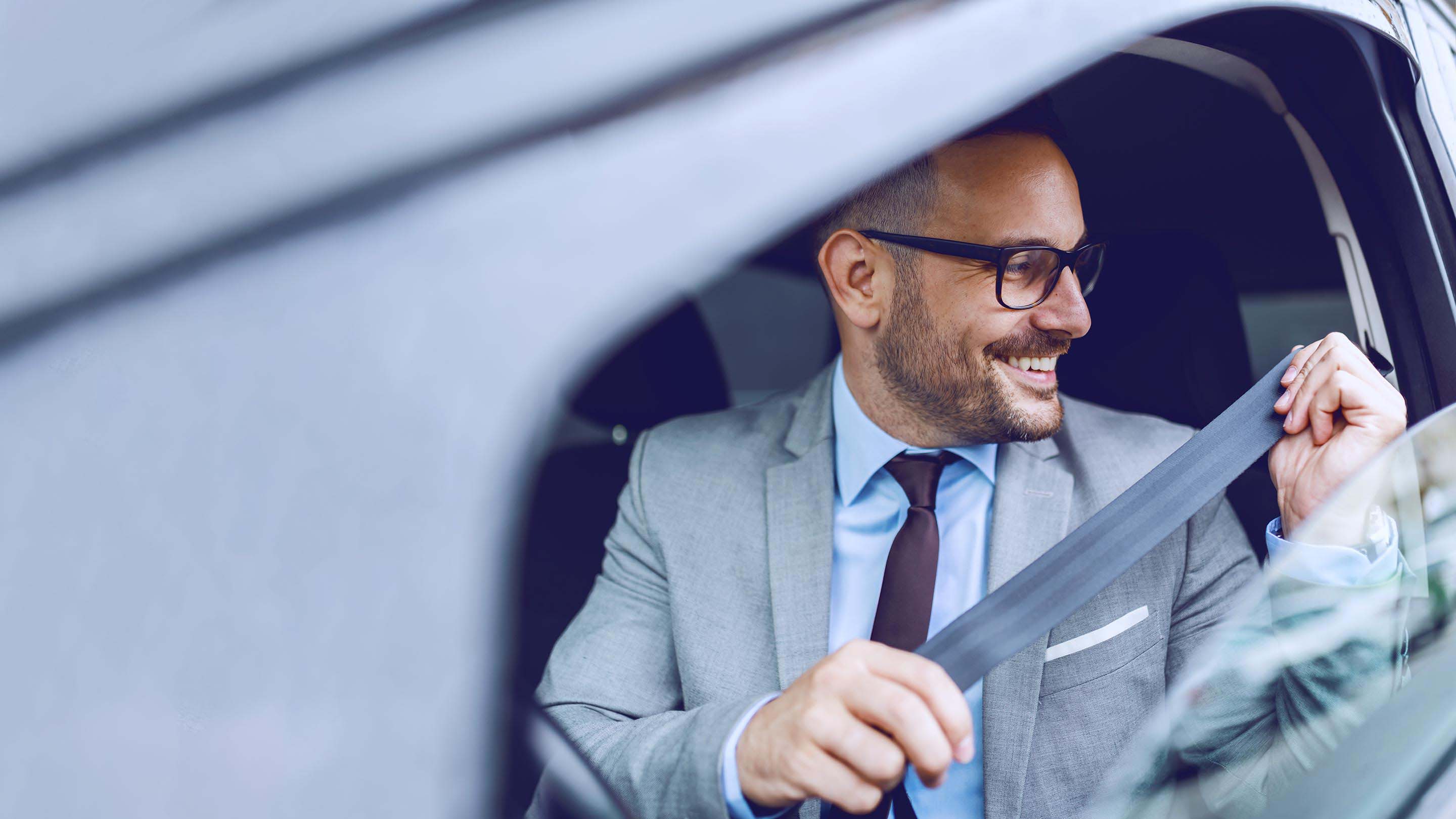 A man in glasses smiling and putting on seatbelt