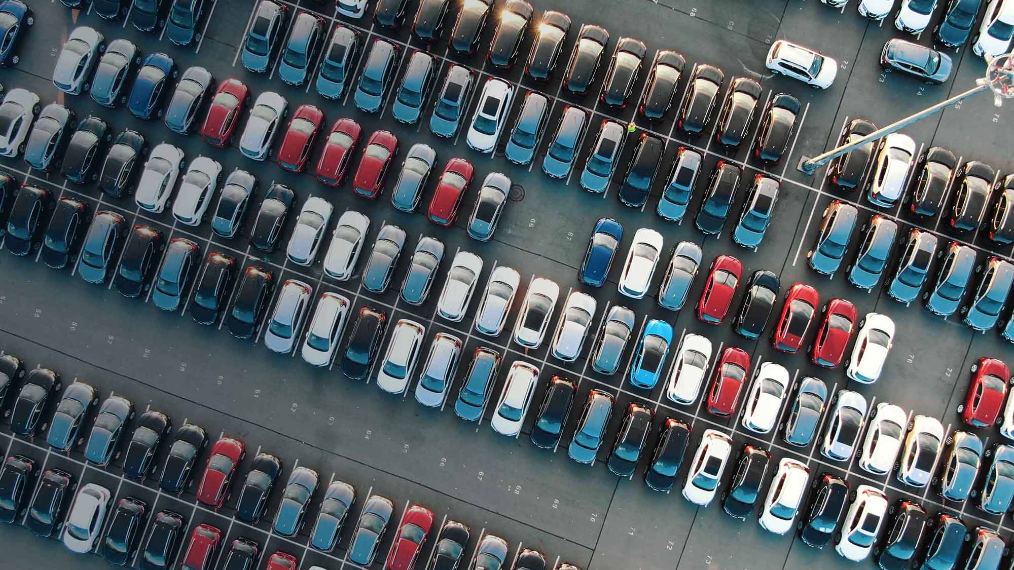 Vehicles of all different colours parked beside each other in parking lot