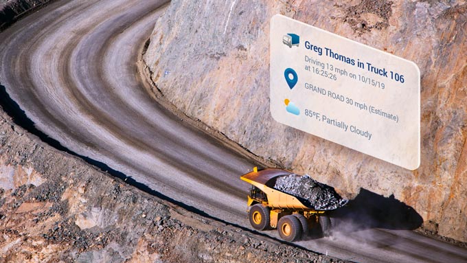 Yellow dump truck driving up a curving dirt road with MyGeotab UI elements above it