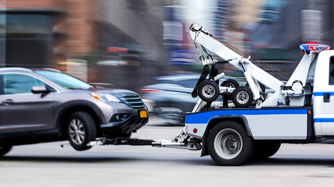 Grey SUV being towed on a busy street by a blue an dwhite tow truck